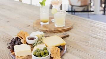 A wooden table with a cheese board, olives, crackers, and drinks.