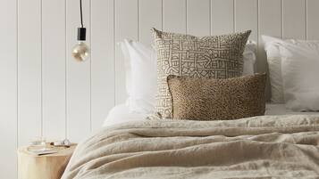 A neatly made bed with patterned pillows, a bedside table with a glass of water, and a hanging light bulb.