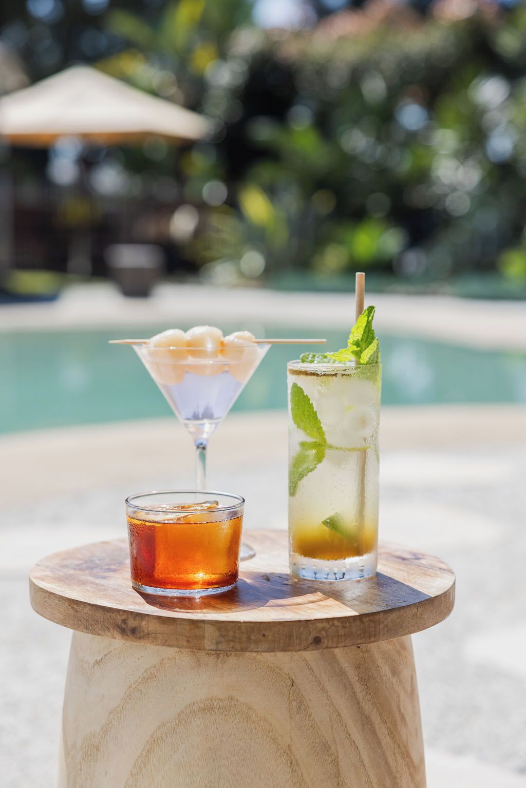 Dos bebidas sobre una mesa de madera junto a una piscina.