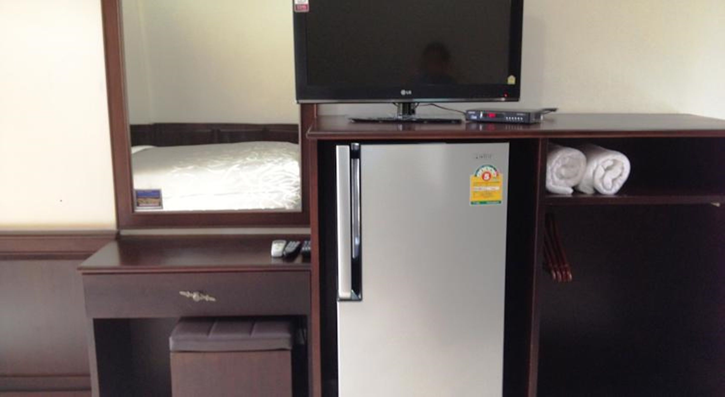 A hotel room with a bed, a TV, a refrigerator, and a small trash bin.