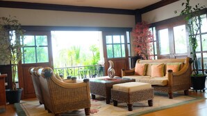A spacious room with a large sofa, two armchairs, and a coffee table. There are large windows providing a view of greenery outside. - Northstar Hotel and Resort (Chiang Rai)