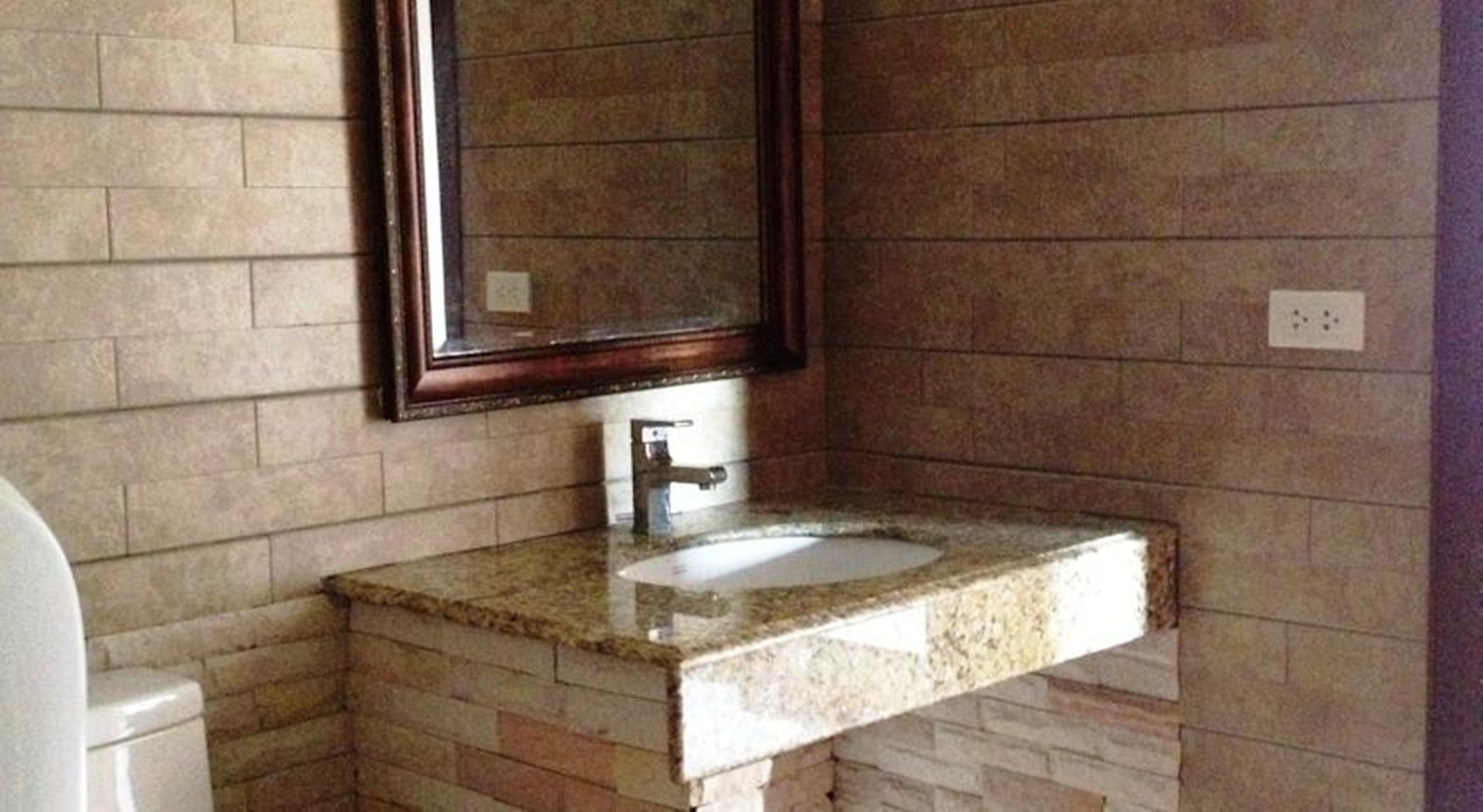 Un baño con pared de piedra, lavamanos con espejo y retrete.