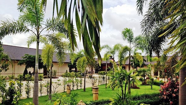 A courtyard with palm trees, a water feature, and a building with a tiled roof. - Northstar Hotel and Resort (Chiang Rai)