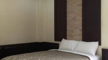 A hotel room with a bed, dark wooden headboard, a brick accent wall, and a plain white wall.