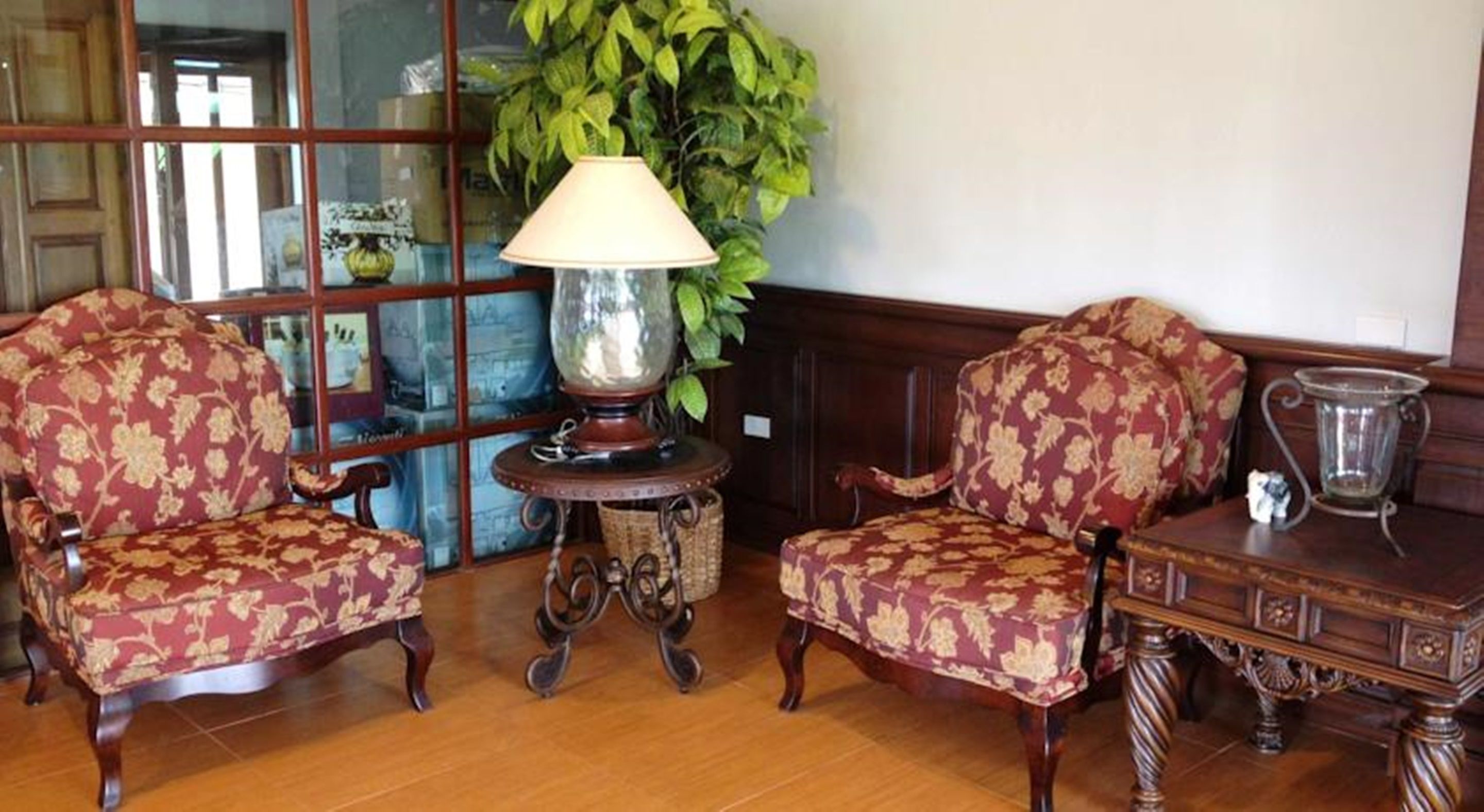 Een kamer met twee versierde fauteuils, een tafeltje met een lamp en een grote potplant.