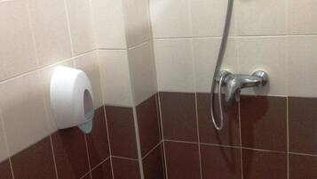 Esquina de un baño con dispensador de toallas de papel y cabezal de ducha.