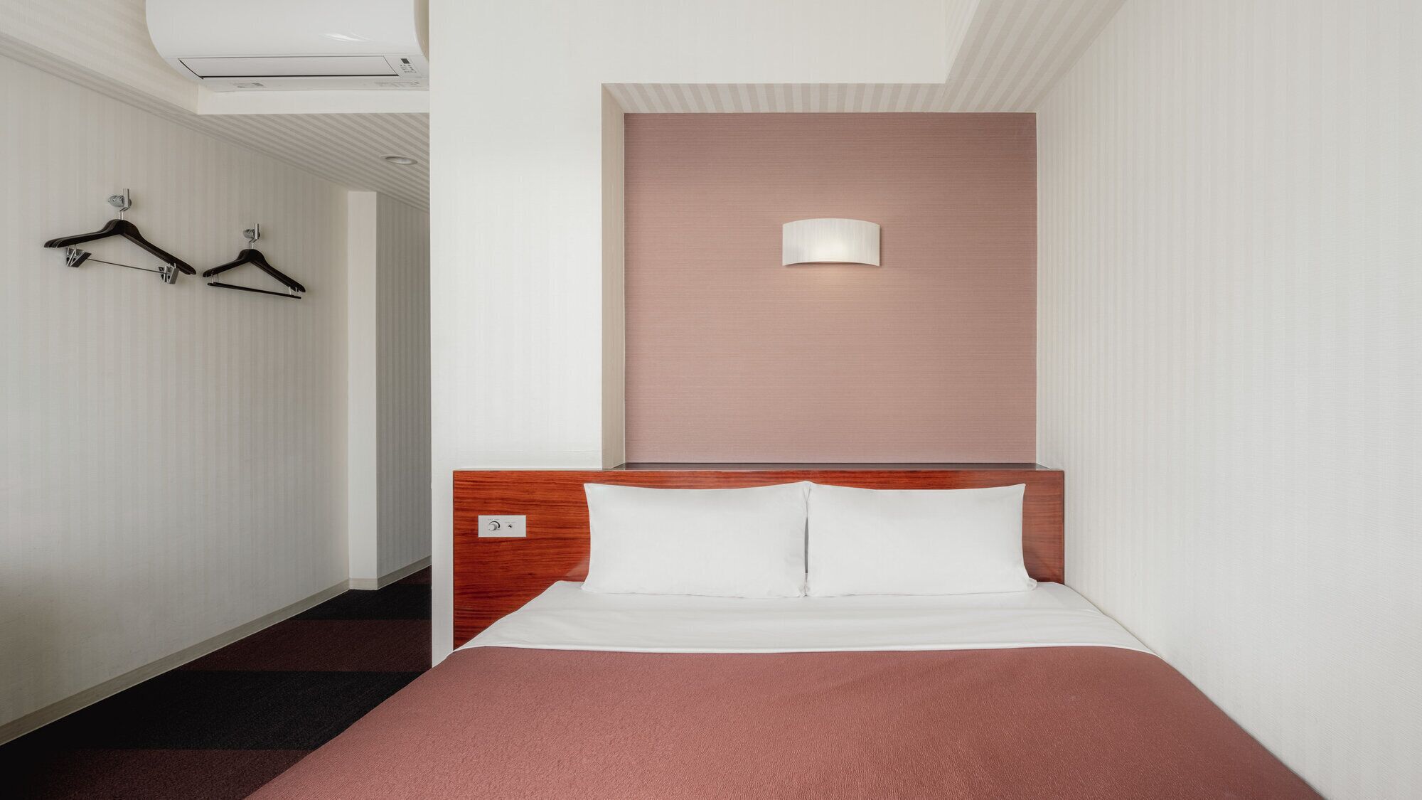 Una habitación de hotel con una cama, una lámpara en la pared y un perchero.