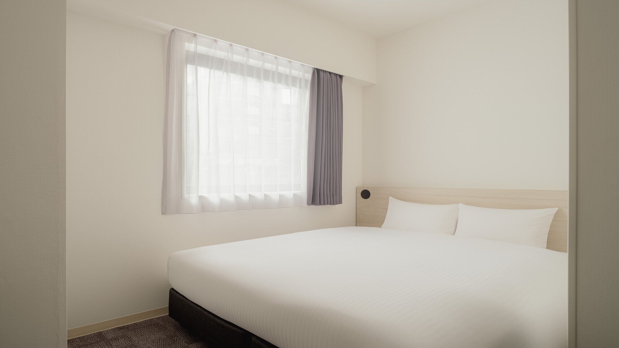 Una habitación de hotel con una cama, una ventana con cortinas translúcidas y un cabecero.