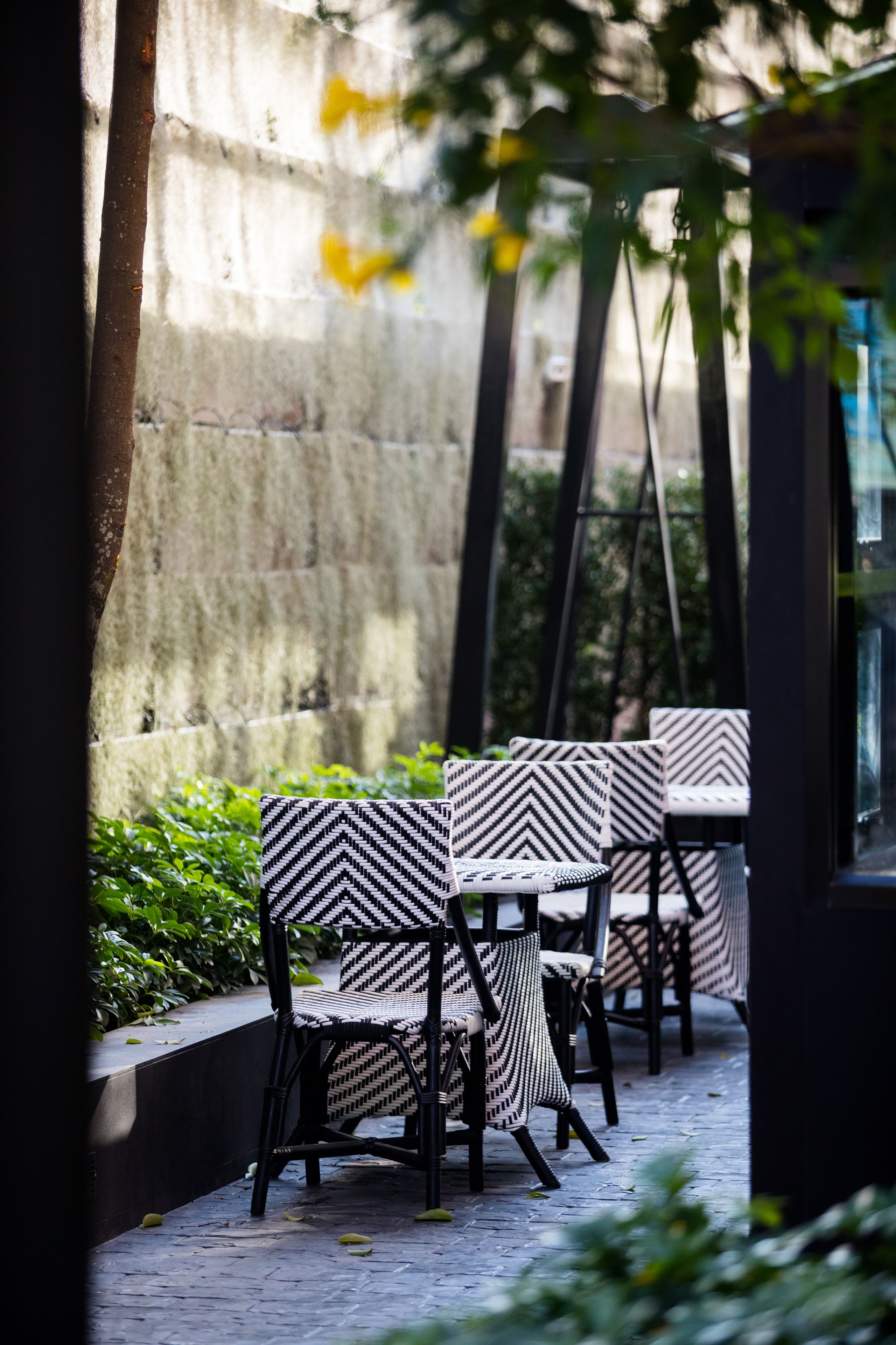 Outdoor seating with black and white patterned chairs and tables, set against a stone wall with greenery.