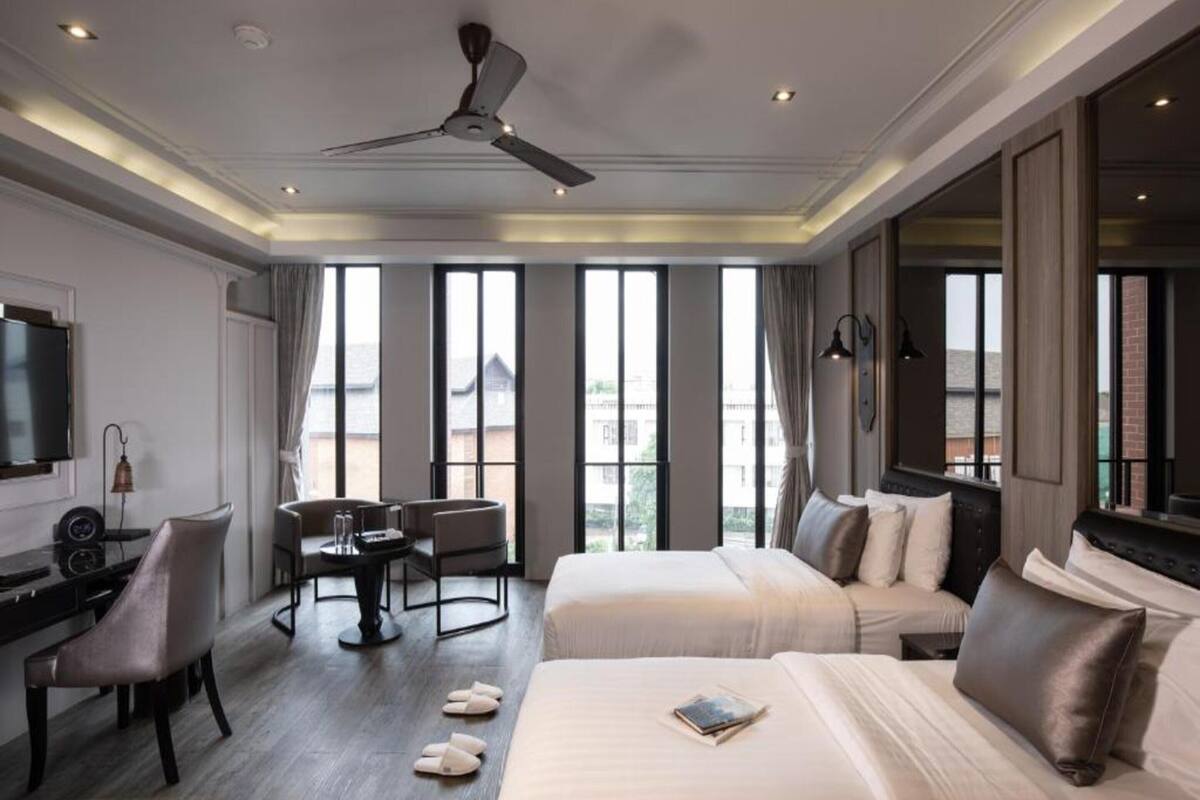 Ein Hotelzimmer mit zwei Betten, einem Schreibtisch, einem Sessel, einem Fernseher und großen Fenstern.