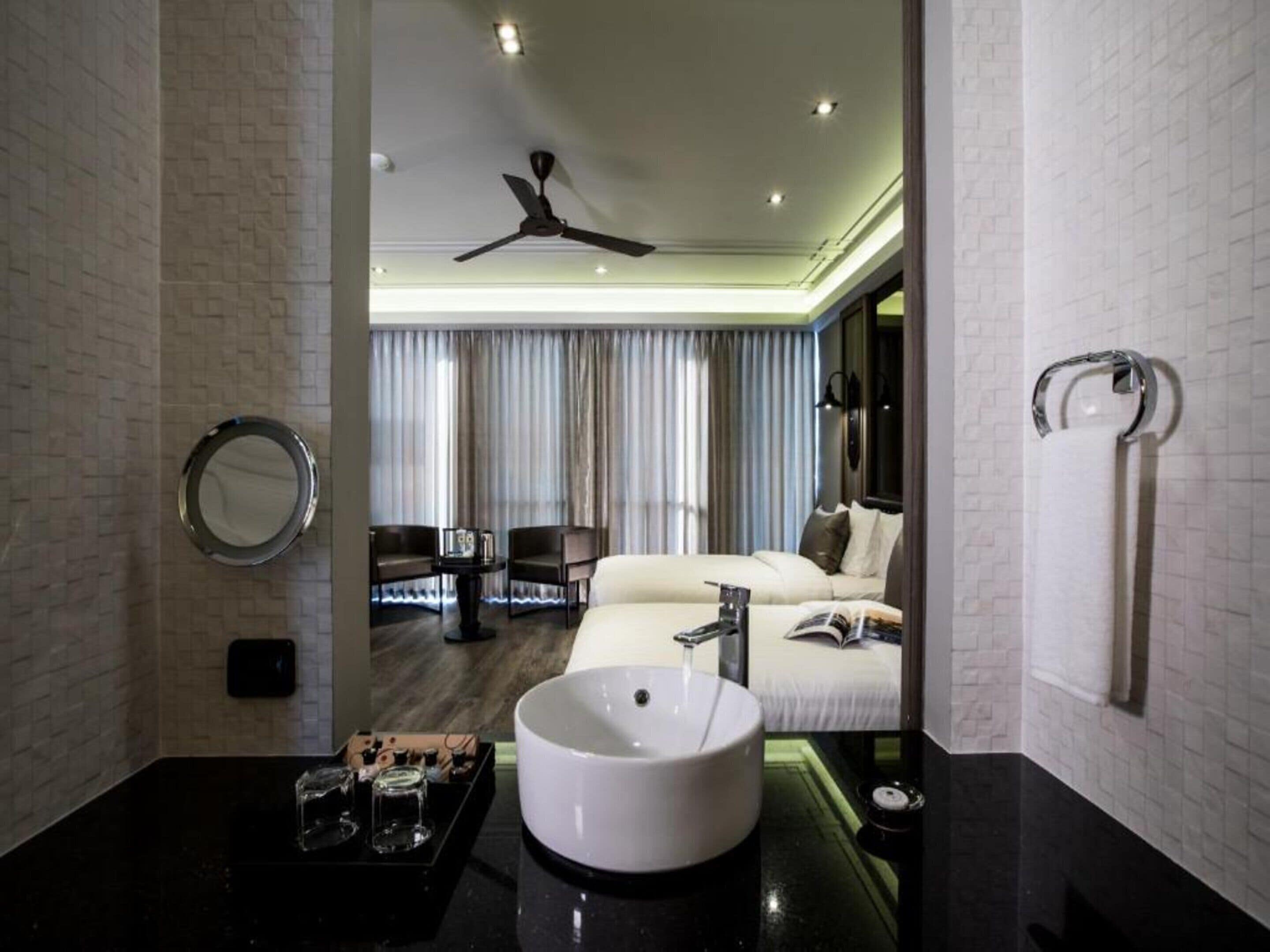 A modern bathroom with a round sink, a ceiling fan, and a view of a living area with a sofa and curtains.