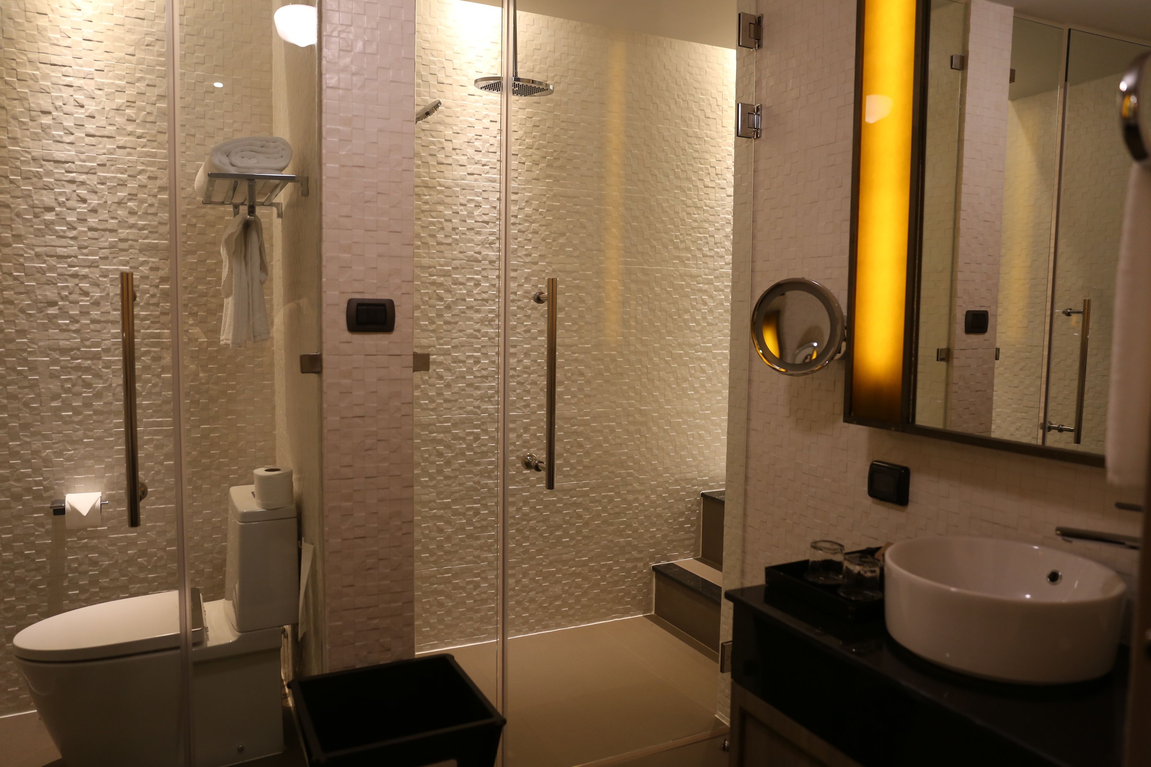 Een moderne badkamer met een douchecabine van glas, een wit toilet, een wastafel en een spiegel met geel licht.