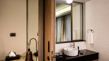 A modern bathroom with a wooden door, a round sink, a mirror, and a towel rack.