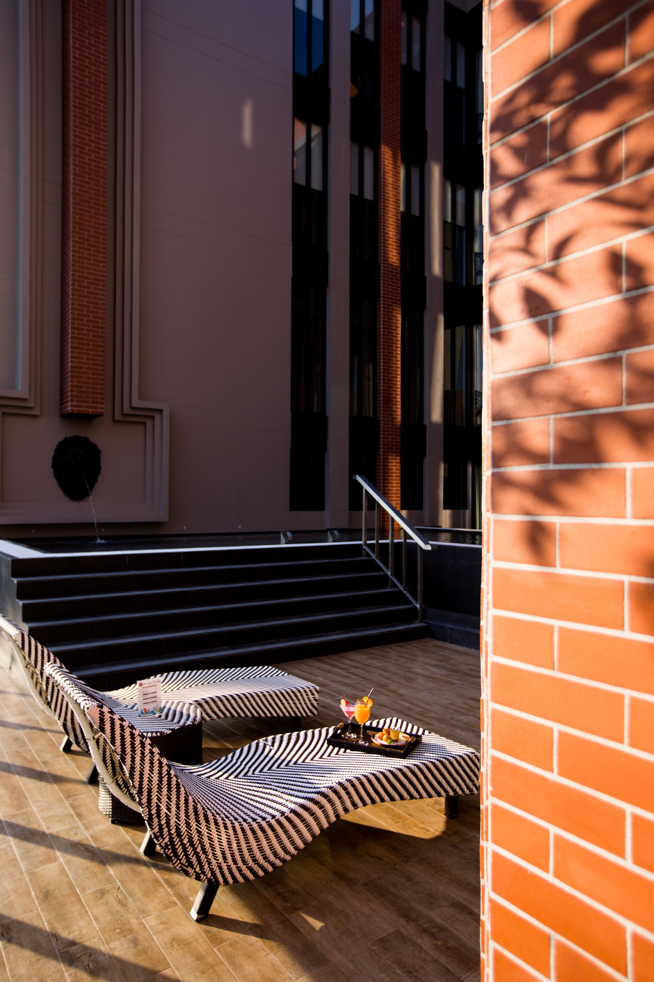 Un área de estar moderna al aire libre con sillones reclinables con diseños, una mesa, una escalera y un muro de ladrillo.