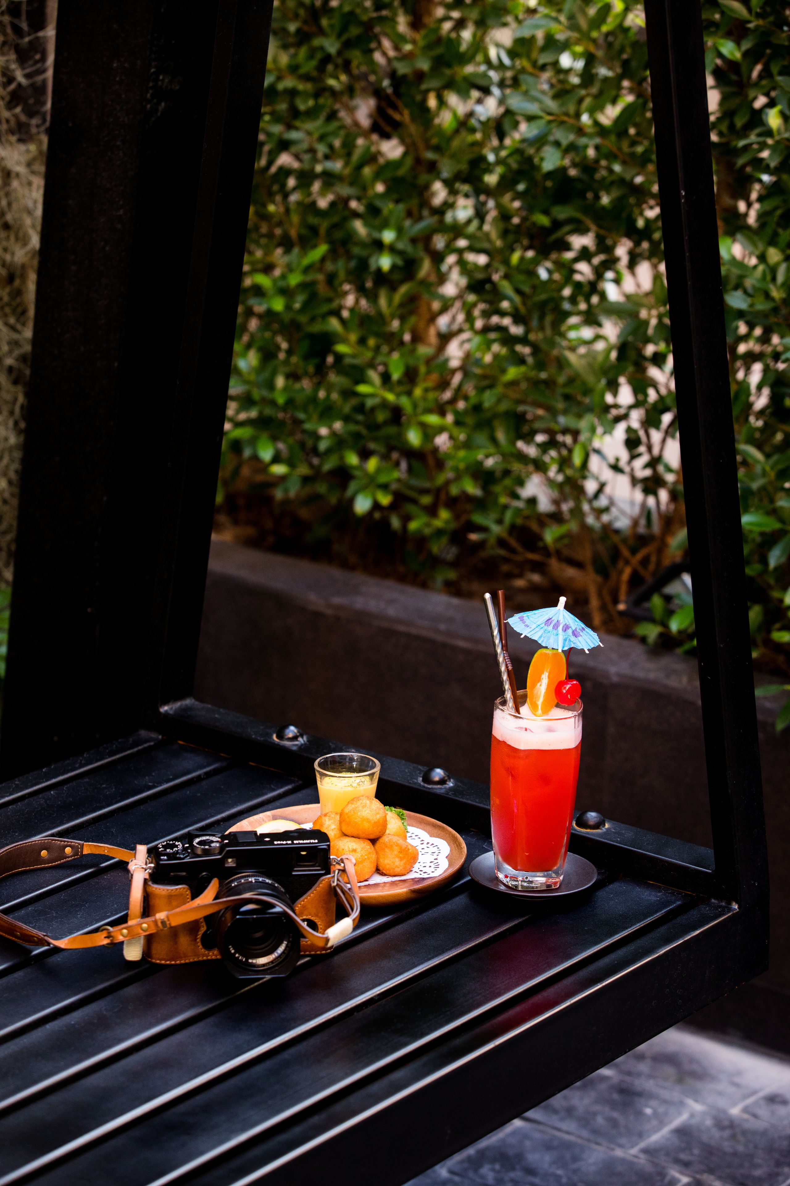 A camera on a bench with a drink and fruit.