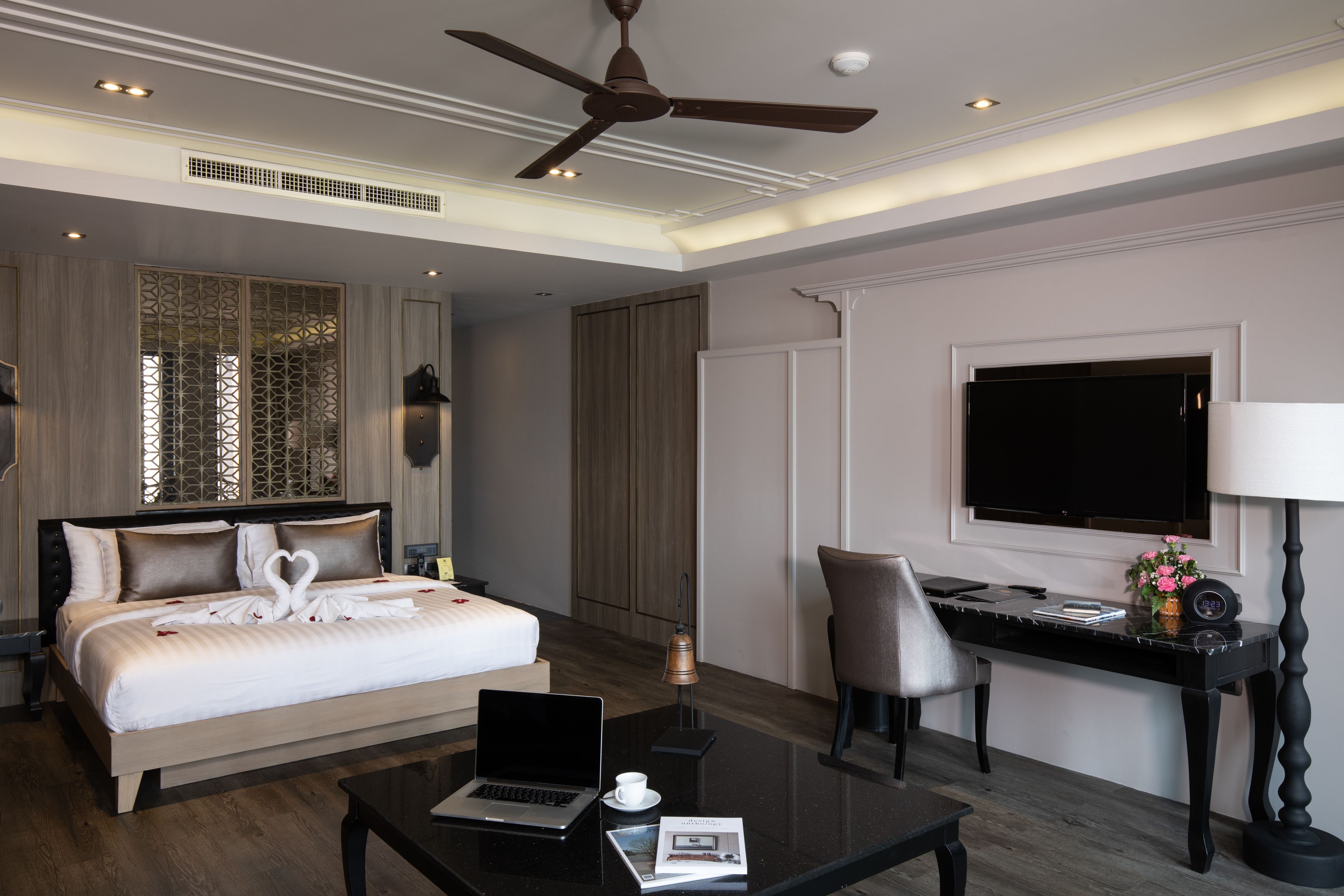 Quarto de hotel moderno com uma cama grande, uma escrivaninha com um laptop, uma cadeira, uma TV e um ventilador de teto.