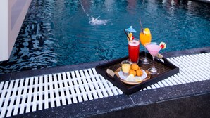 Ein Pool auf dem Dach mit Getränken und Snacks, umgeben von einem modernen Gebäude mit großen Fenstern und einer Ziegelaußenwand.