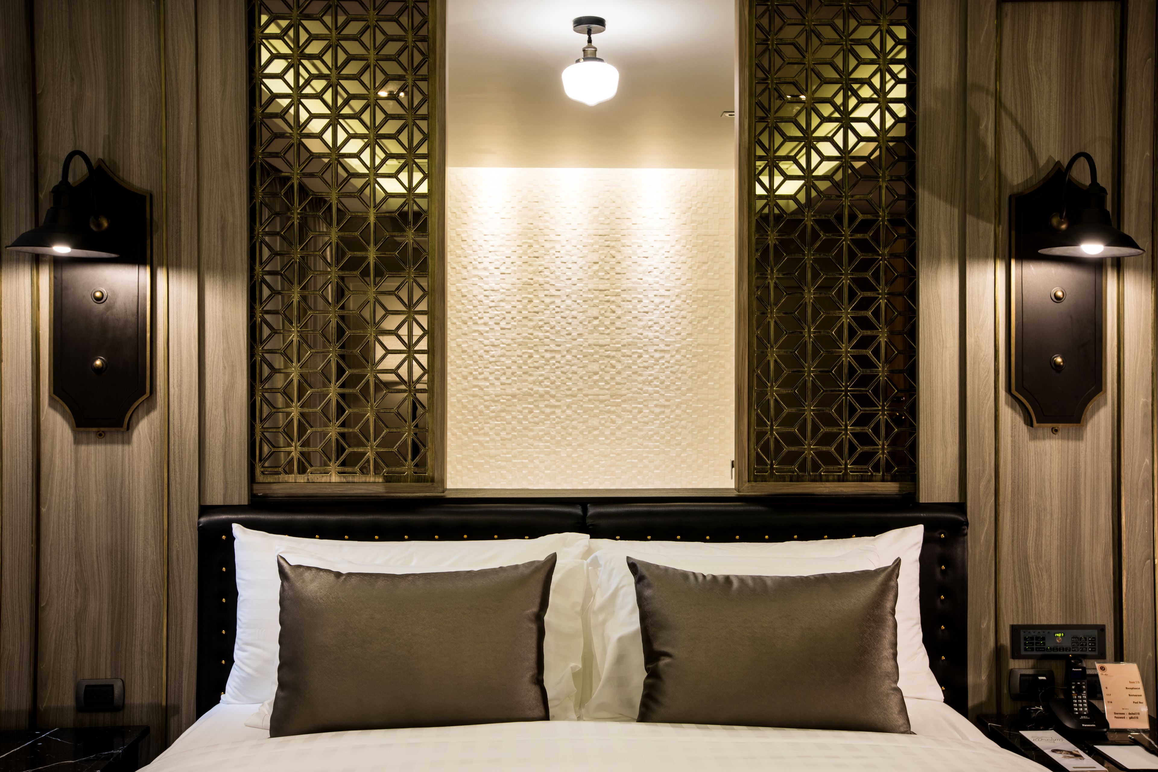 A hotel room with a bed, two wall-mounted lamps, a decorative screen, and a ceiling light.
