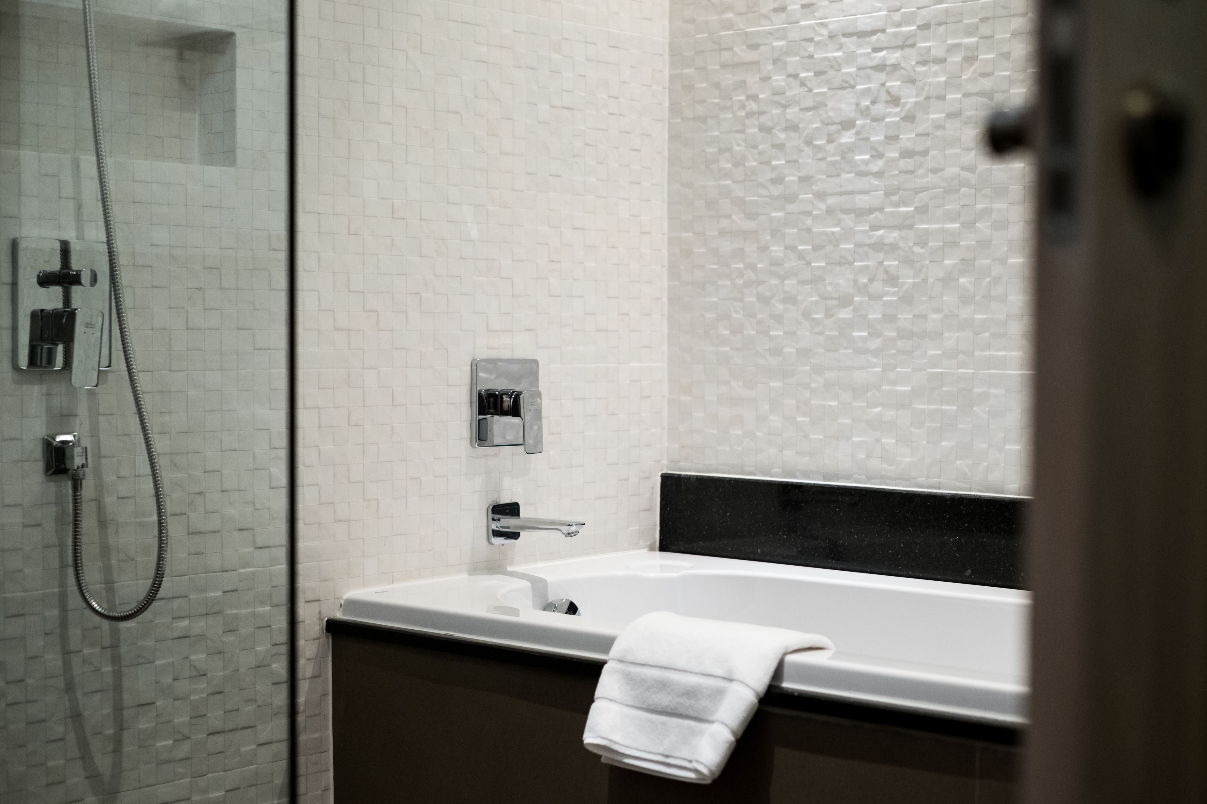 A modern bathroom with a glass-enclosed shower, a white tiled wall, a black countertop, and a white towel hanging on the edge.