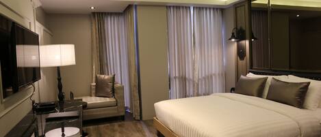 A hotel room with a bed, a desk with a lamp, a chair, and a television.