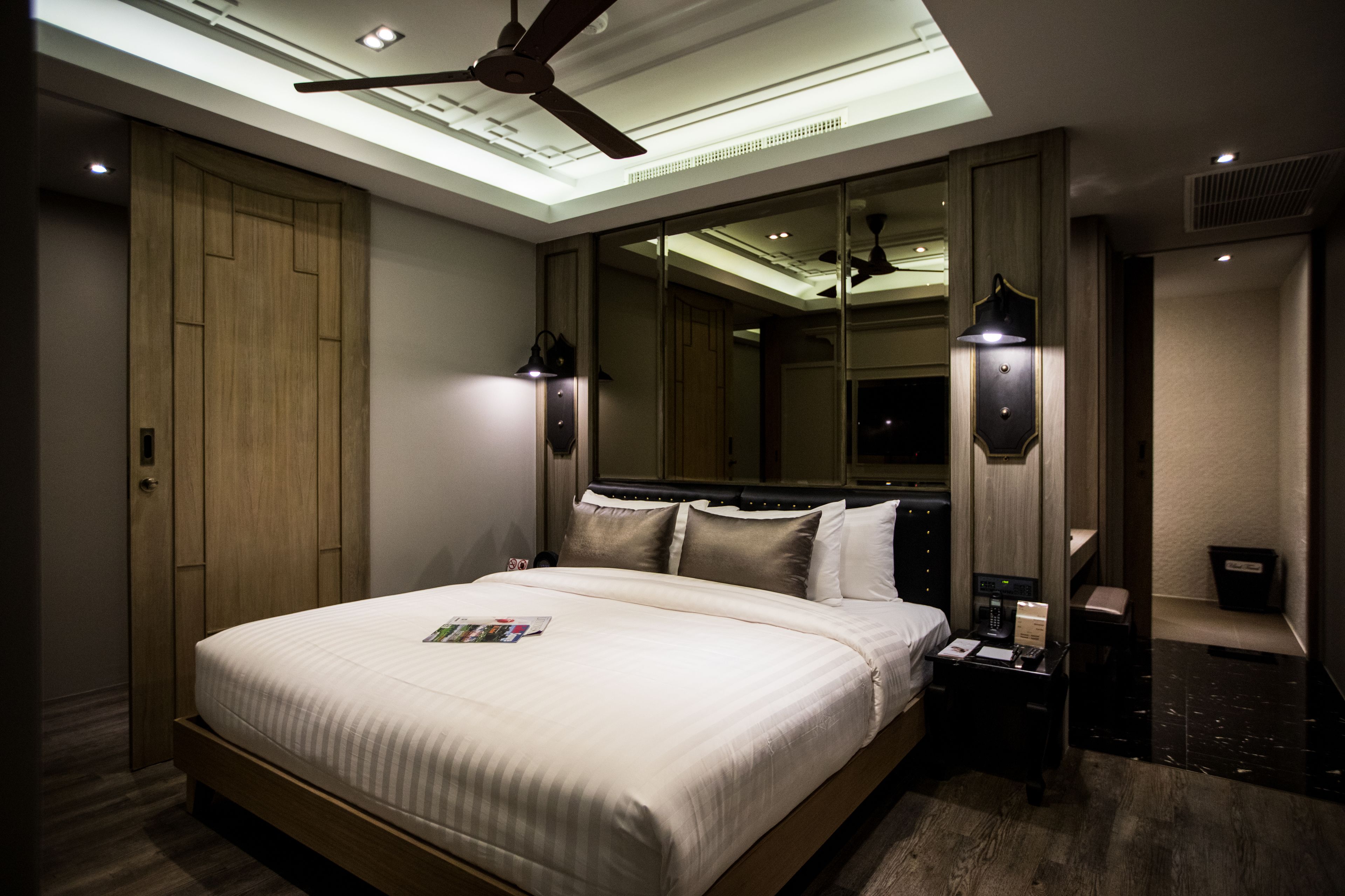 Habitación de hotel moderna con una cama grande, ventilador de techo, tragaluz y mesita de noche con lámpara.