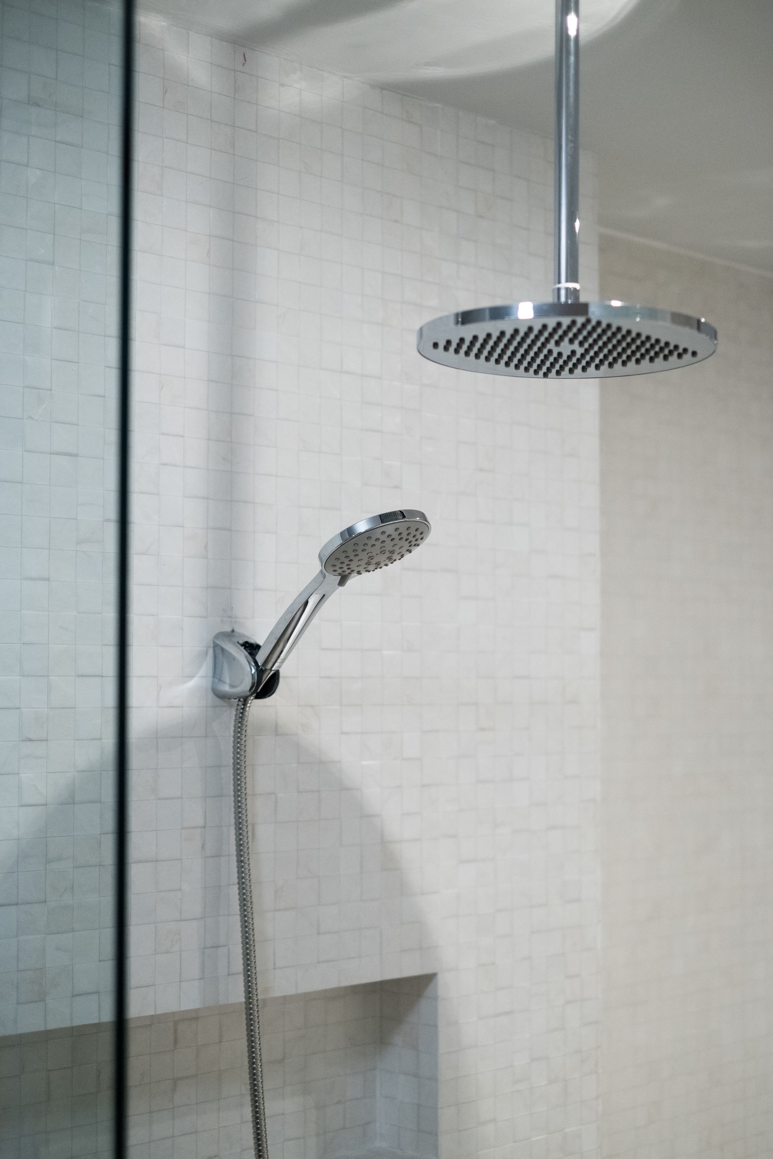 Ducha con cabezal de ducha manual y otro fijo en la pared cubierta de azulejos.