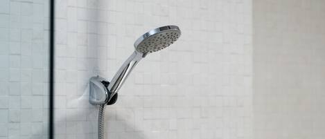 Ducha con cabezal de ducha manual y otro fijo en la pared cubierta de azulejos.