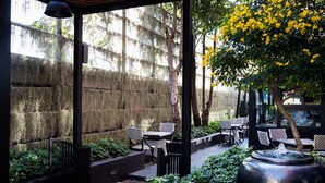 Eine Terrasse im Freien mit schwarzen Metallgeländern, einer Steinmauer und einer Sitzgelegenheit mit karierten Tischen und Stühlen.