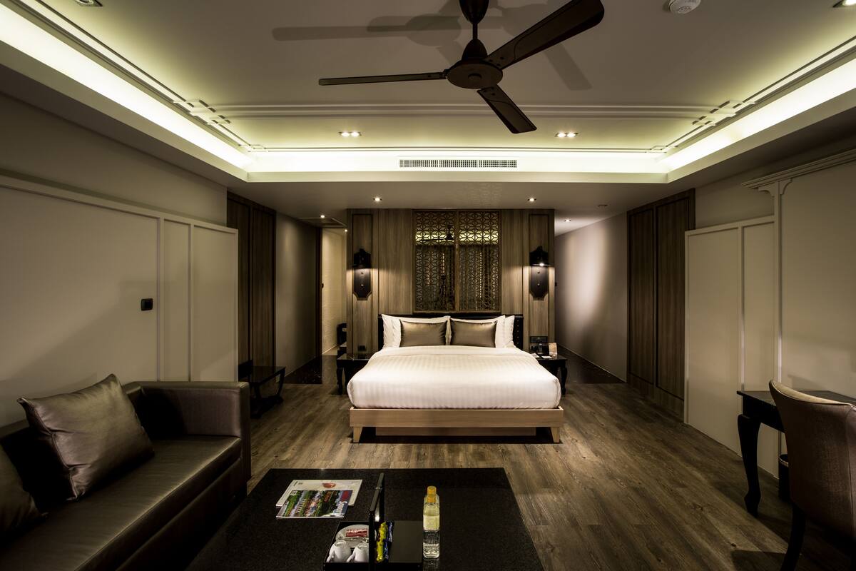 Ein modernes Hotelzimmer mit einem großen Bett, einer Sitzecke, einem Couchtisch und einem Deckenventilator.