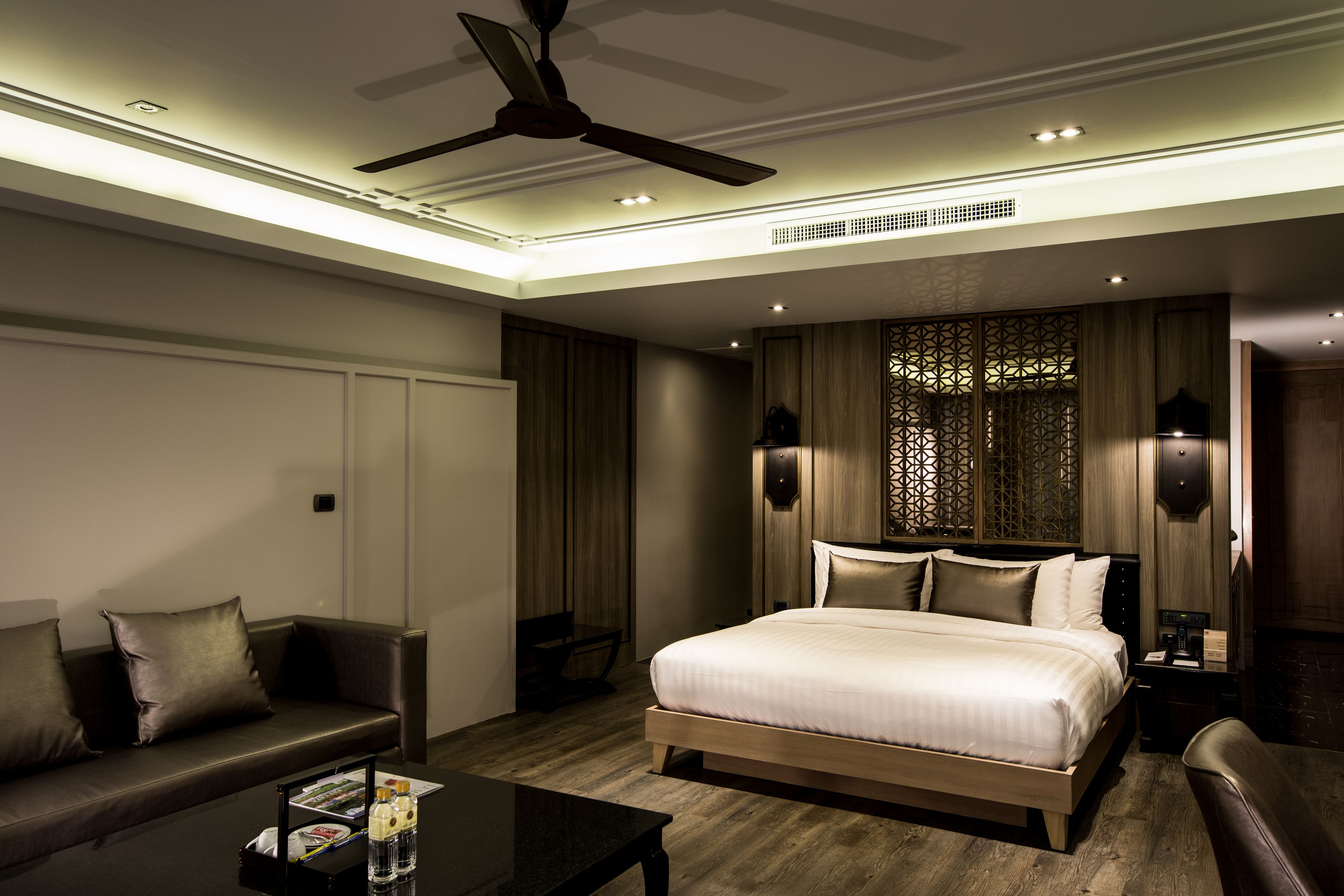 Una habitación de hotel moderna con una cama grande, un sofá, una mesa de centro y un ventilador de techo.