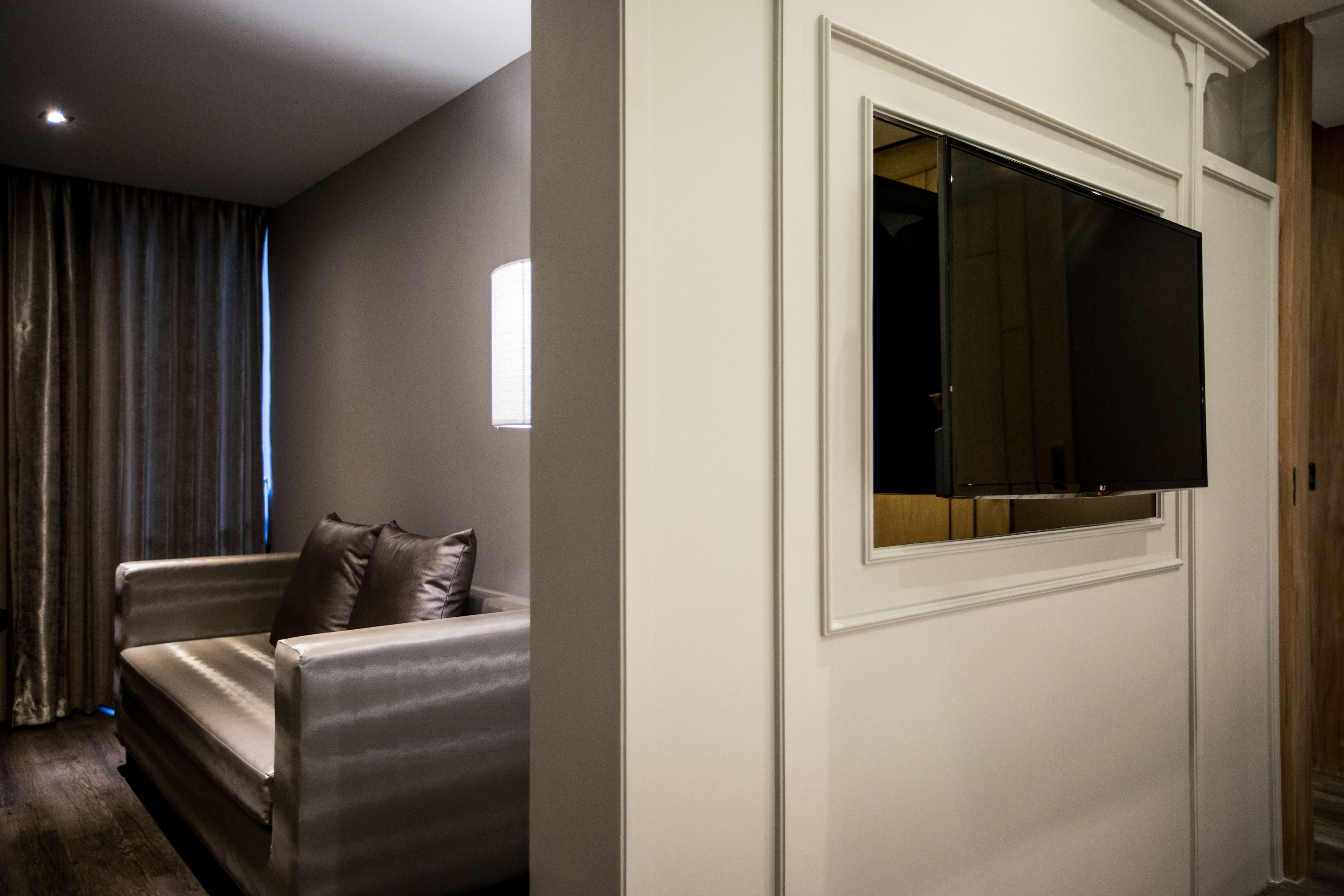 A modern living room with a sofa, a flat-screen TV mounted on a wall, and a window with curtains.