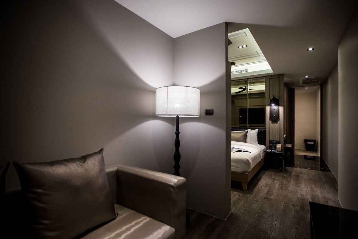 Een hotelkamer met een bed, nachtkastje, lamp en uitzicht op de gang.