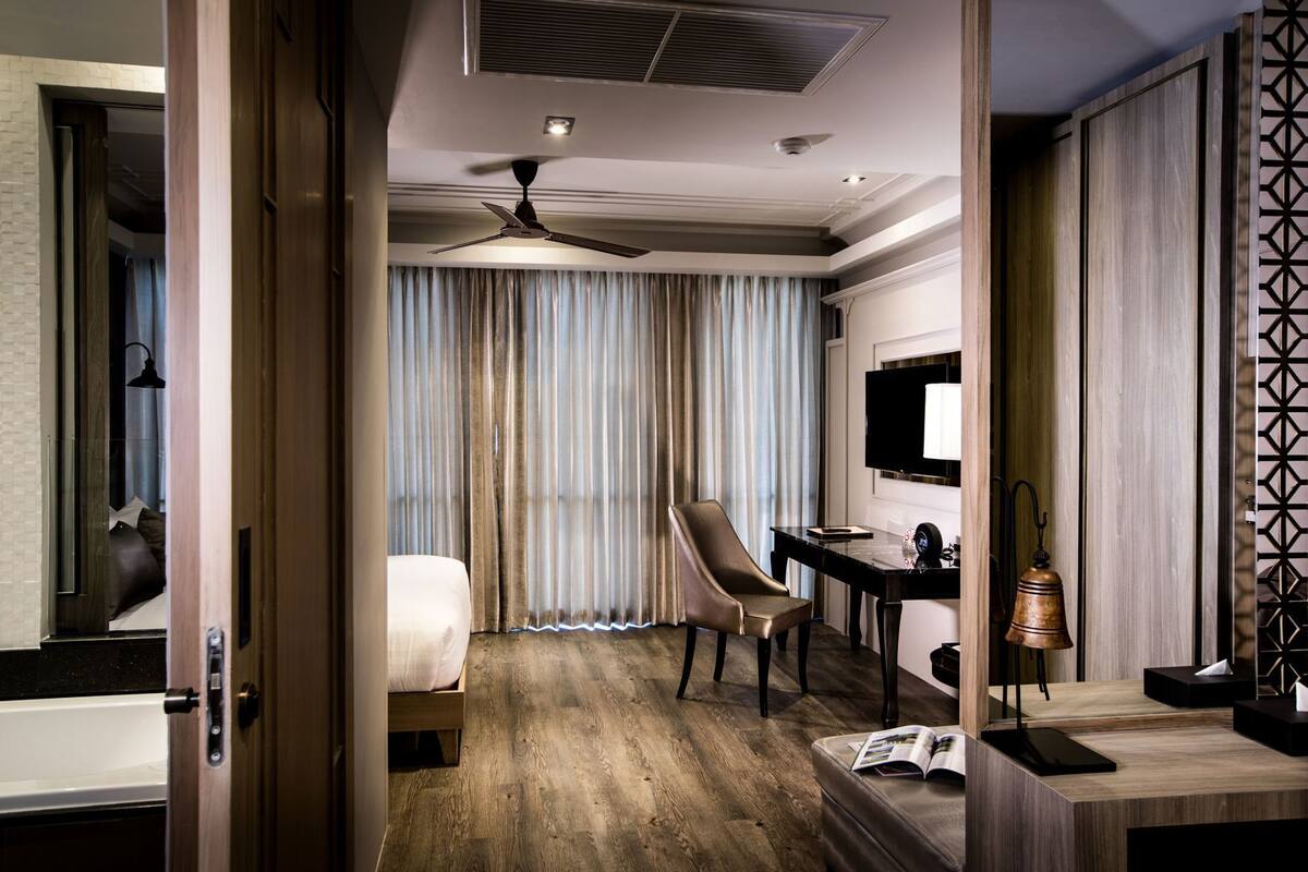 Ein Hotelzimmer mit Bett, Schreibtisch, Stuhl, Deckenventilator, Fernseher und einer Wandverkleidung.