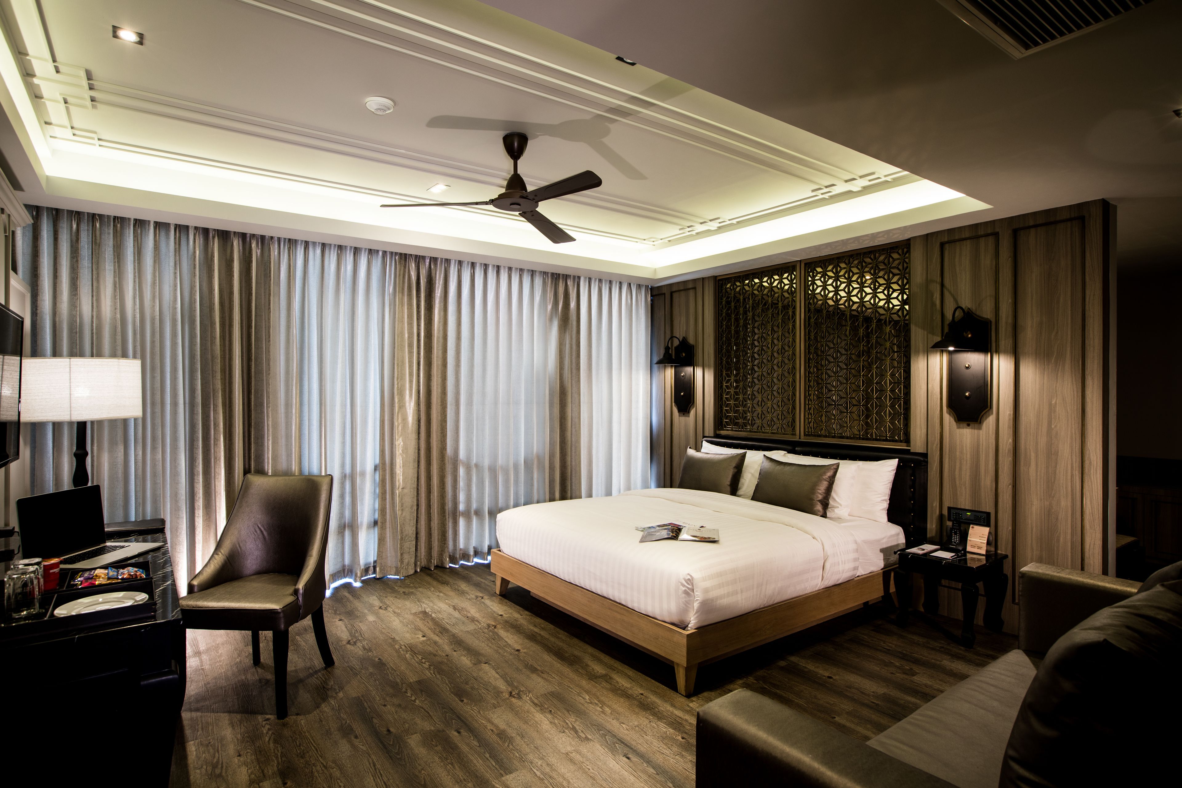 A modern hotel room with a large bed, a desk with a laptop, a chair, and a ceiling fan.