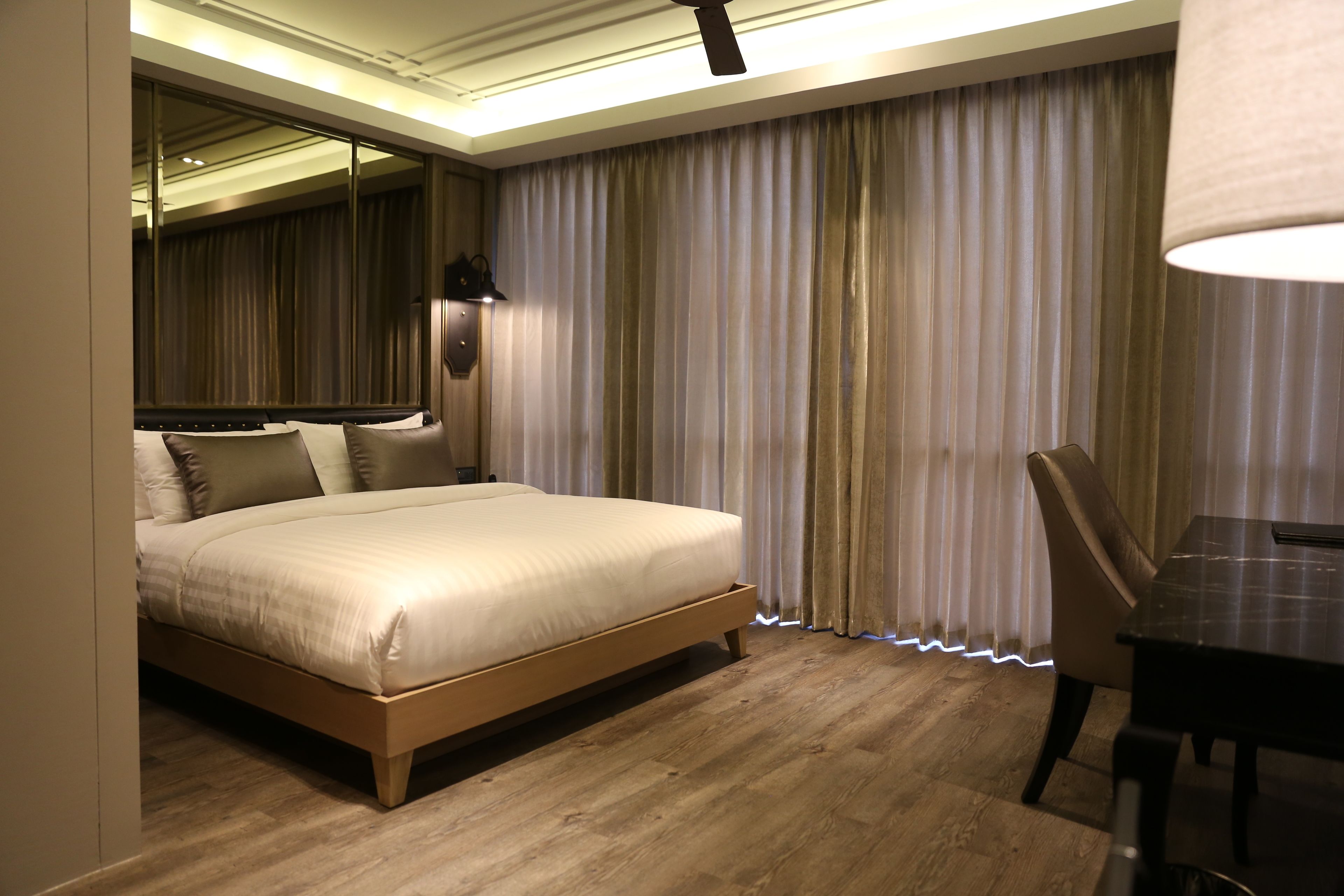 Een moderne hotelkamer met een groot bed, een eettafel en uitzicht door dunne gordijnen.