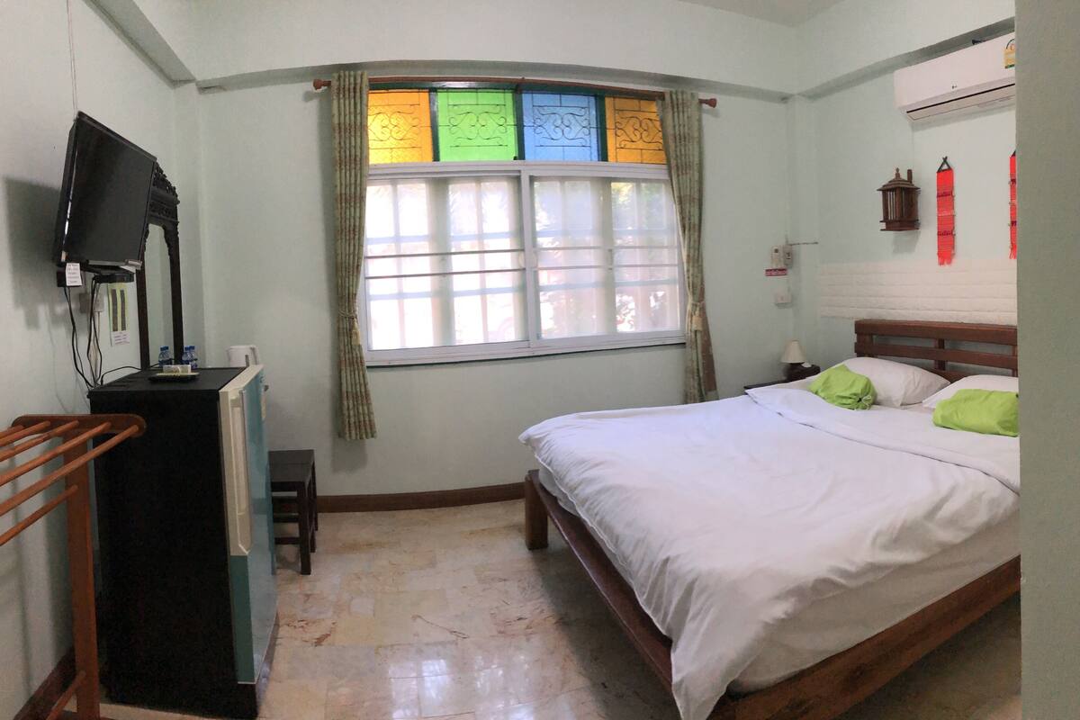 A bedroom with a bed, a desk, a television, and a window with curtains.