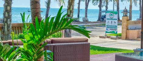 A view of a beachside area with palm trees, a signboard, and a paved walkway.