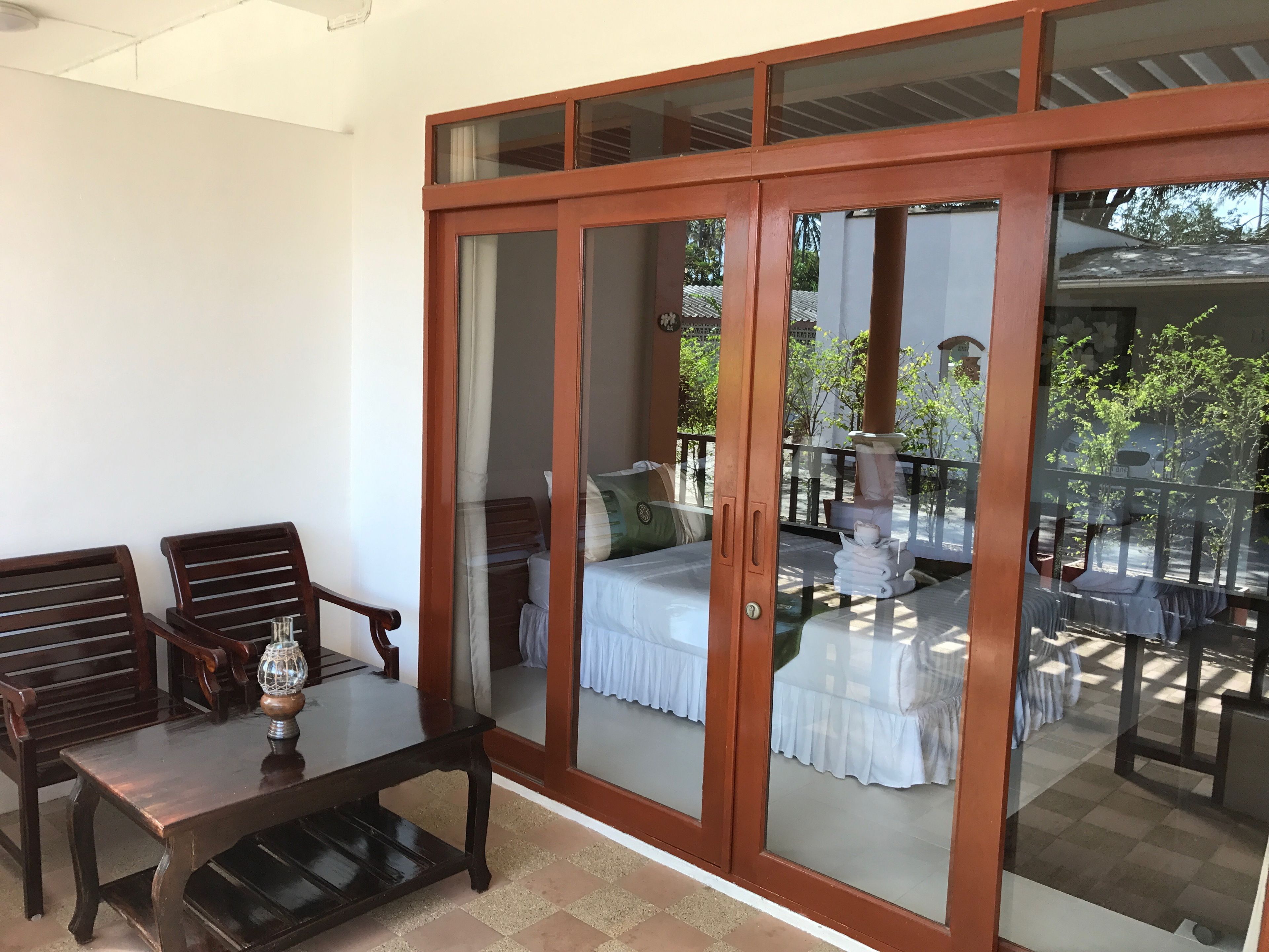 A room with a wooden table and chairs, a bed with a white bedspread, and a balcony with a railing.