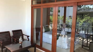 A room with a wooden table and chairs, a bed with a white bedspread, and a balcony with a railing.
