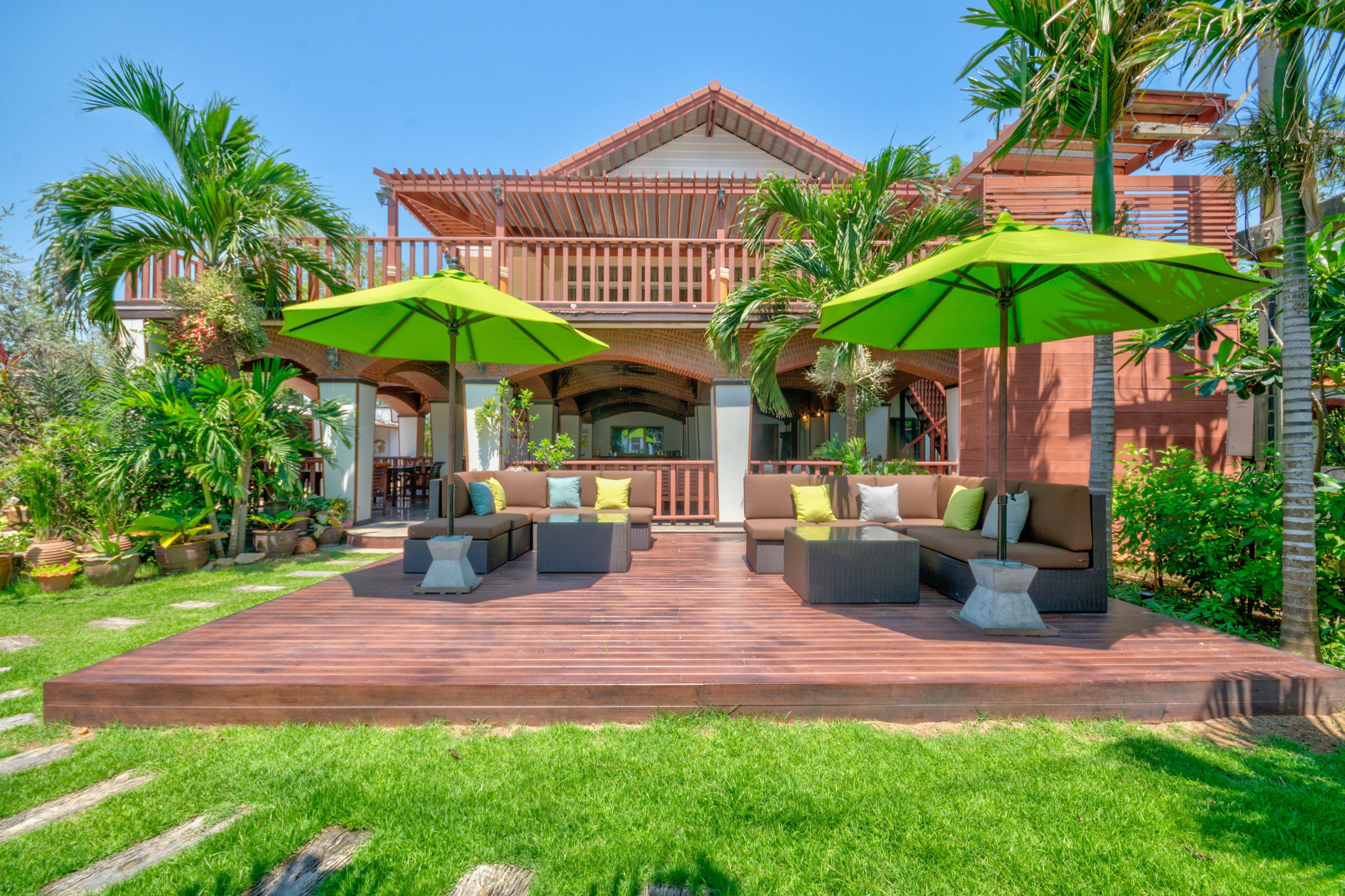 Amplia terraza al aire libre con varias zonas de estar, rodeada de exuberante vegetación y palmeras.