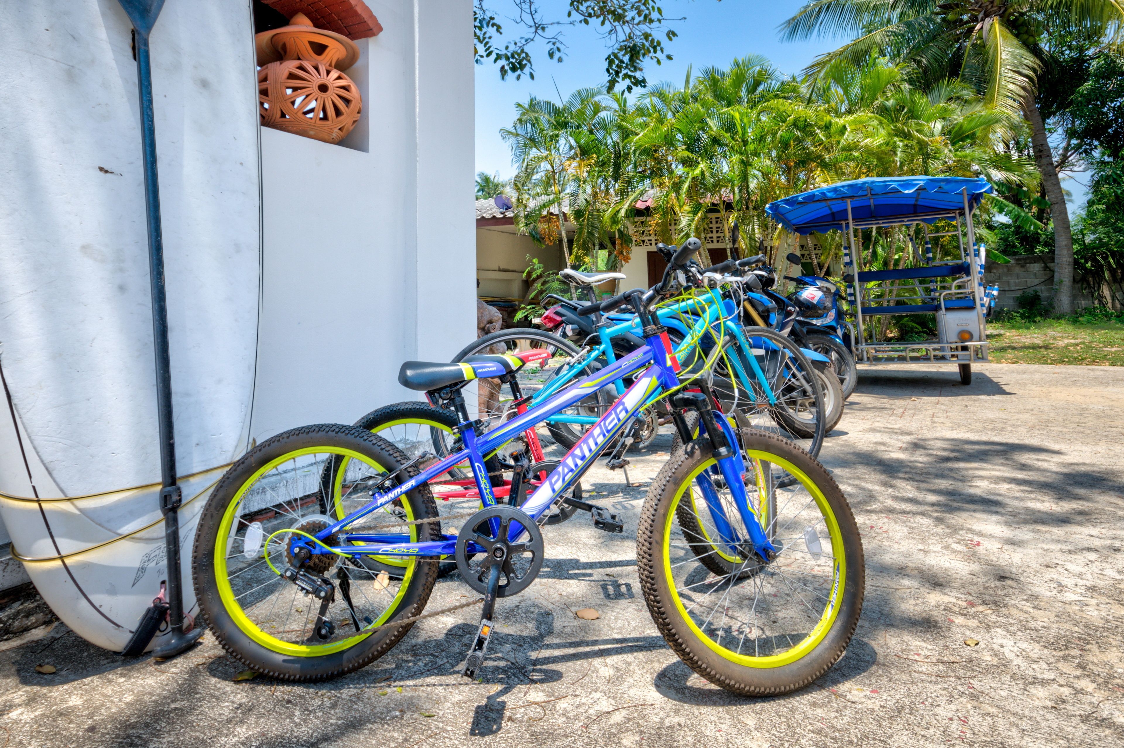 Varias bicicletas estacionadas frente a un edificio de fachada blanca y toldo azul.