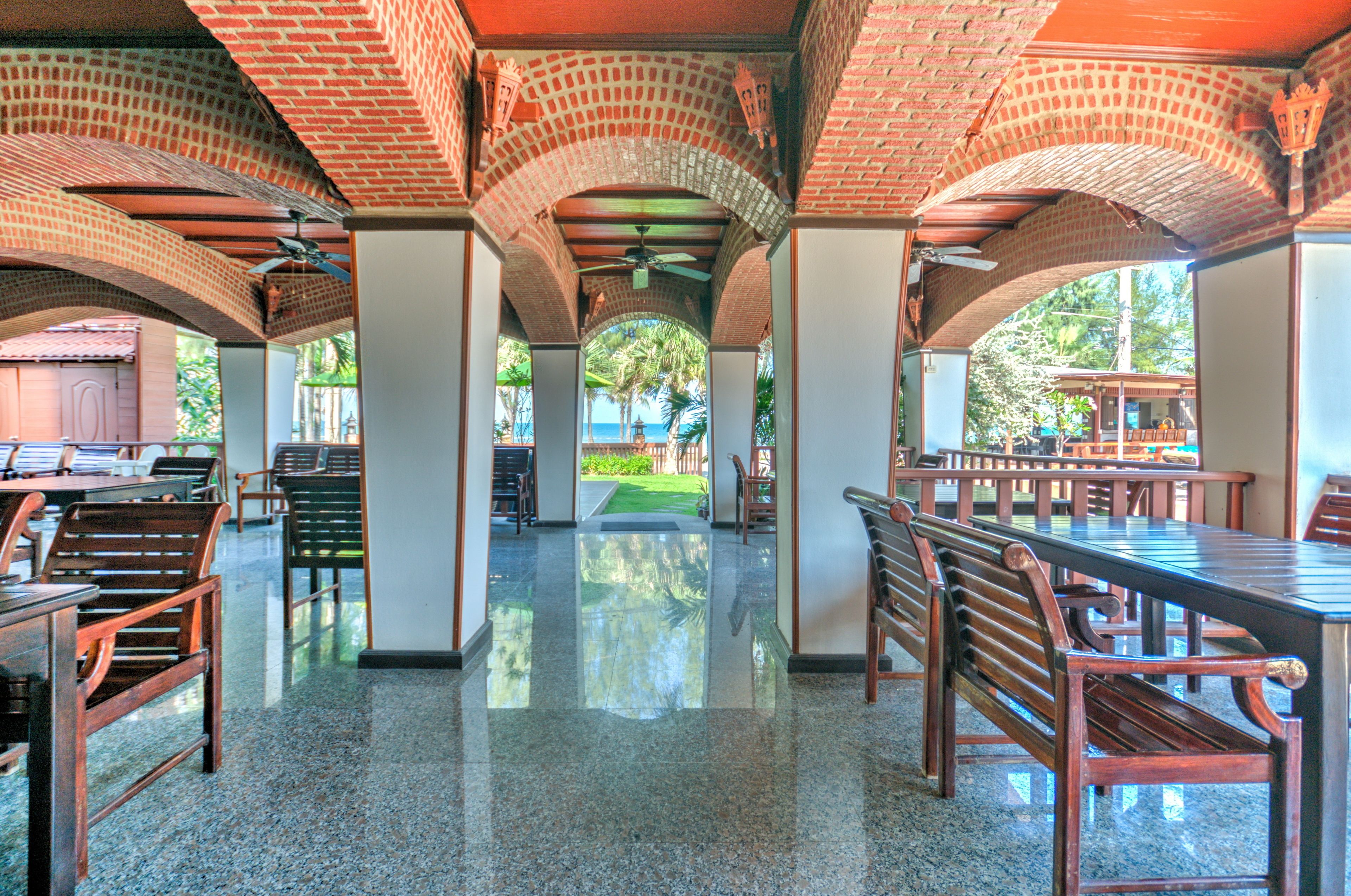 Un área de comedor al aire libre techada con arcos de ladrillo, bancos y mesas de madera.