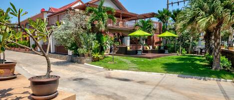 A hotel with a red-tiled roof, a covered patio with a green umbrella, and a well-maintained lawn.