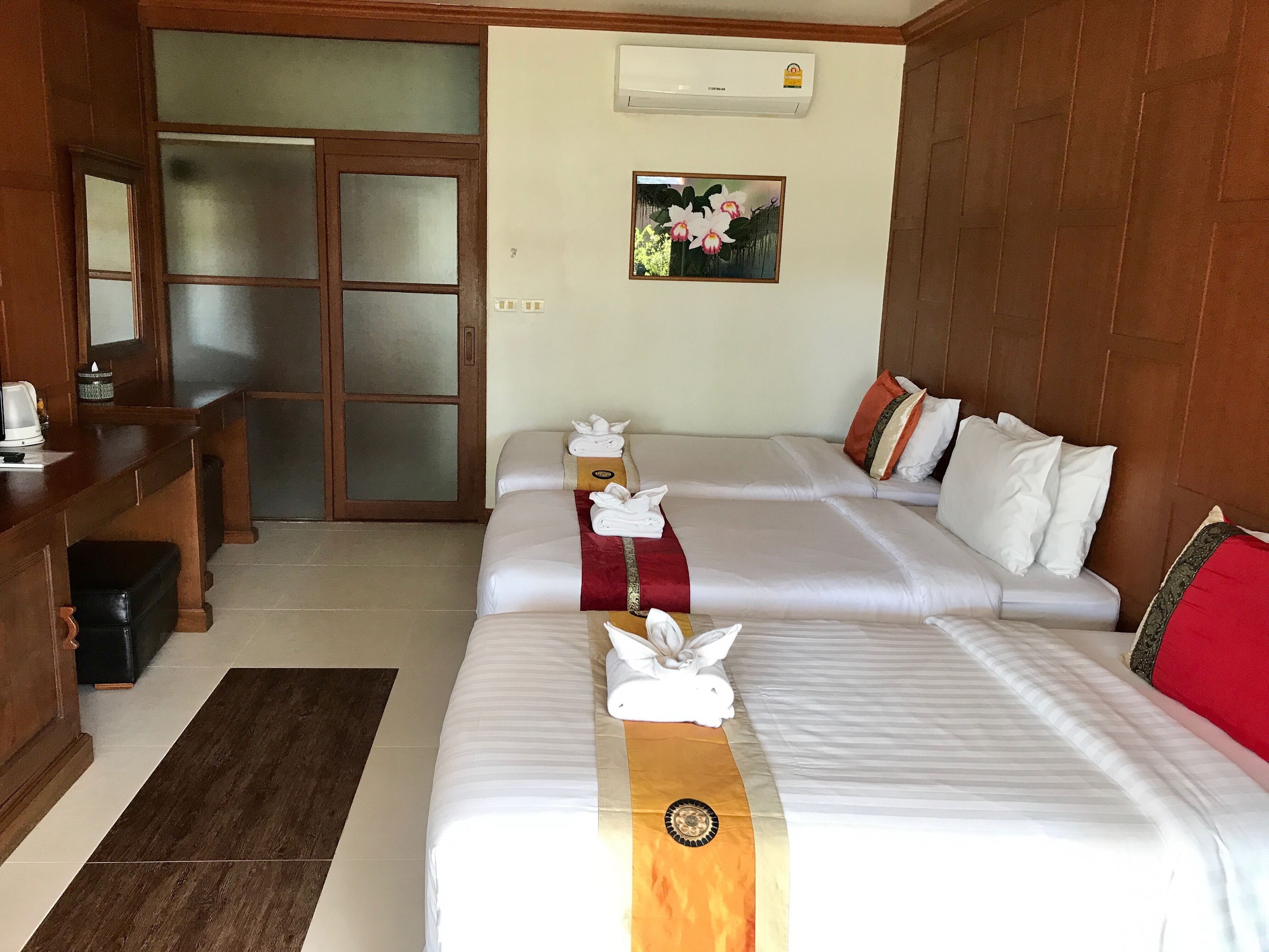 A hotel room with two beds, a wooden desk, a mirror, and a wall-mounted air conditioner.