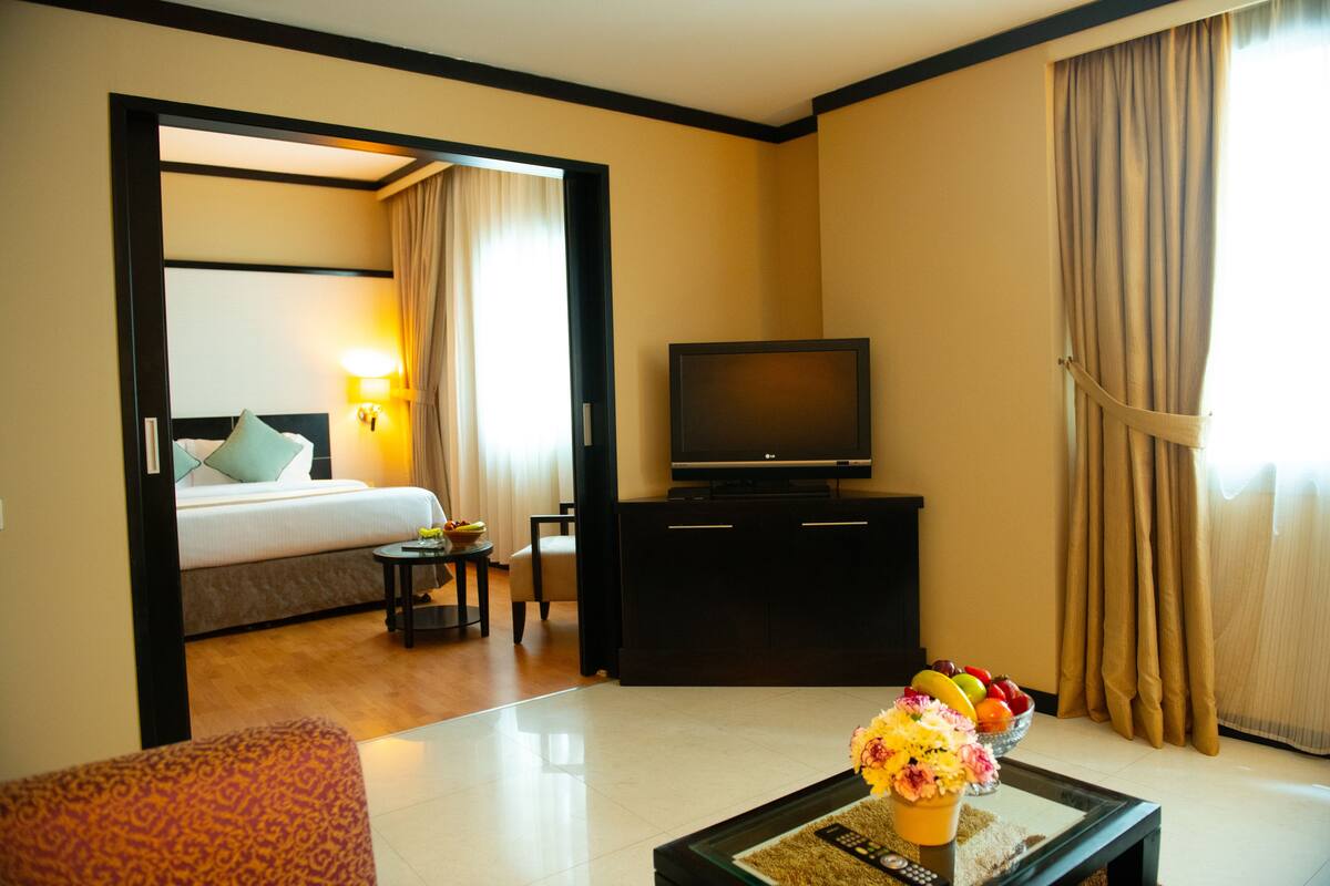 A hotel room with a bed, a television, a coffee table with flowers, and a fruit bowl.