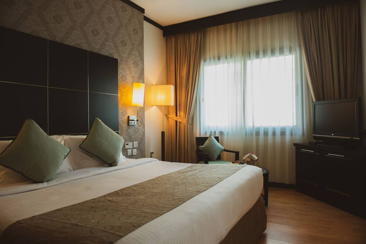 A hotel room with a large bed, two bedside lamps, a television, and a window with curtains.