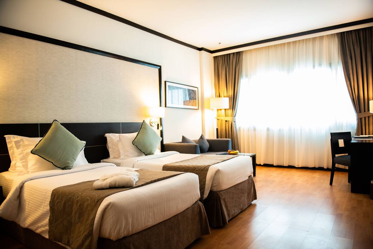 A hotel room with two beds, a desk, and a chair.