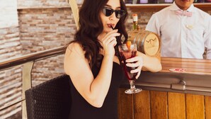 A woman in a black dress sitting at a bar with a bartender. The bar has wooden panels and a brick wall background. - Grandeur Hotel (Dubai)