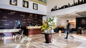 A modern hotel lobby with a reception desk, seating area, and a large decorative vase with flowers. - Grandeur Hotel (Dubai)