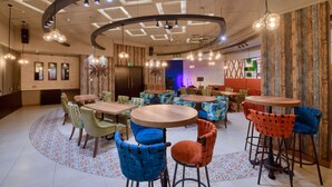 A modern restaurant interior with round tables and chairs, a patterned floor, and a ceiling with exposed beams and hanging lights. - Grandeur Hotel (Dubai)